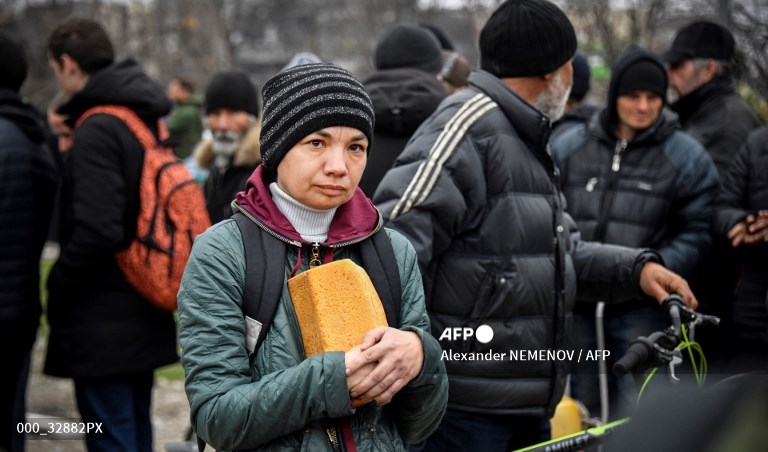 Seorang wanita memegang roti ketika orang-orang mengantre pada distribusi makanan yang diselenggarakan oleh tentara dan sukarelawan Rusia di Mariupol pada 12 April 2022.